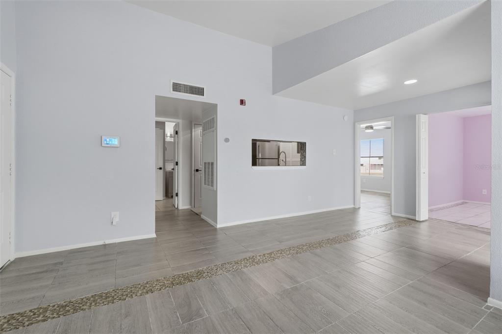 A living area with gray tile flooring, a pass-through window, and doorways to other rooms — 3716 IDLEBROOK CIRCLE UNIT 212, CASSELBERRY, FL