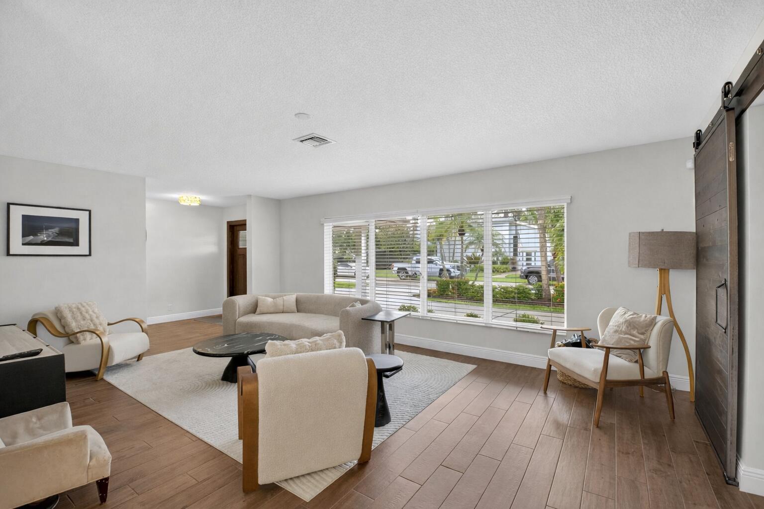 A living room with light wood floors, a curved sofa, armchairs, and a sliding barn door — 650 SW 16th Street, Boca Raton FL 33486, BOCA RATON, FL
