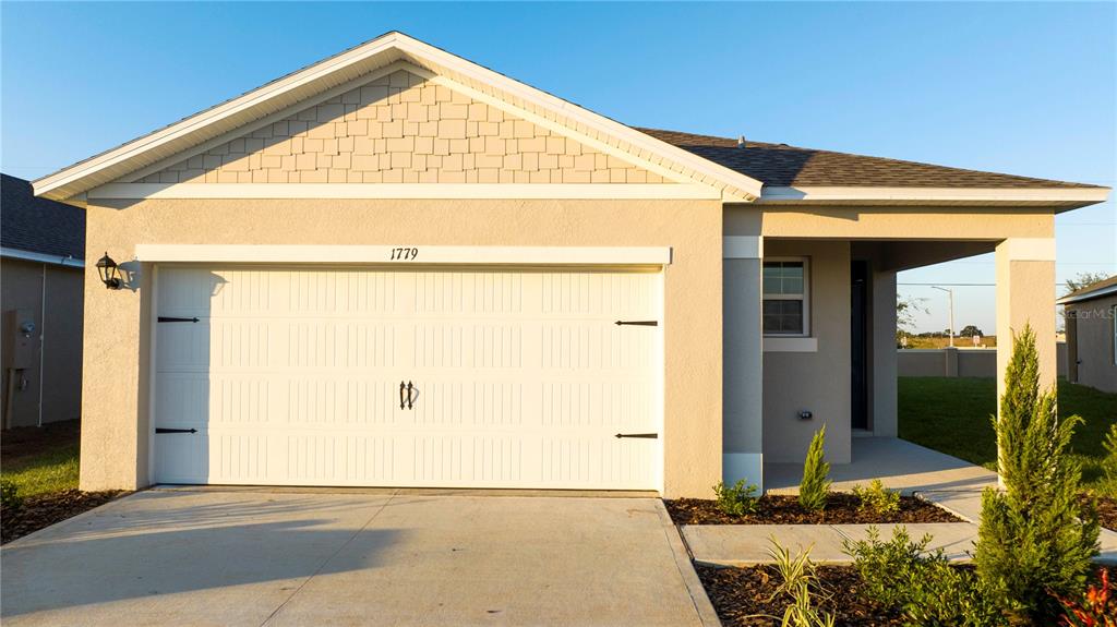 A single-story house exterior features a two-car garage, a covered entryway, and tan siding — 1779 POST OAK DRIVE, DAVENPORT, FL