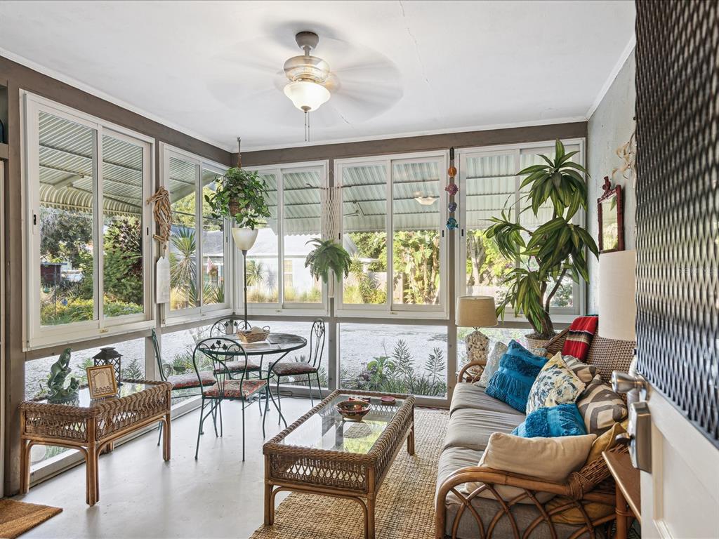 A sunroom features wicker furniture, a ceiling fan, and large windows overlooking a gravel yard — 5638 VIRGINIA AVENUE, NEW PORT RICHEY, FL