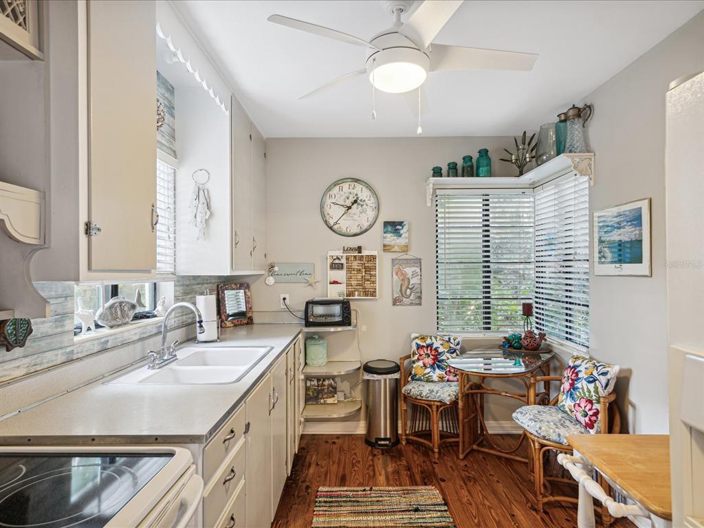 A kitchen features white cabinets, a double sink, a small dining area, and wood flooring — 5638 VIRGINIA AVENUE, NEW PORT RICHEY, FL