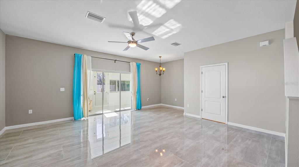An open living area features light gray tile flooring, a ceiling fan, and sliding glass doors — 12843 BUFFALO RUN DRIVE, GIBSONTON, FL