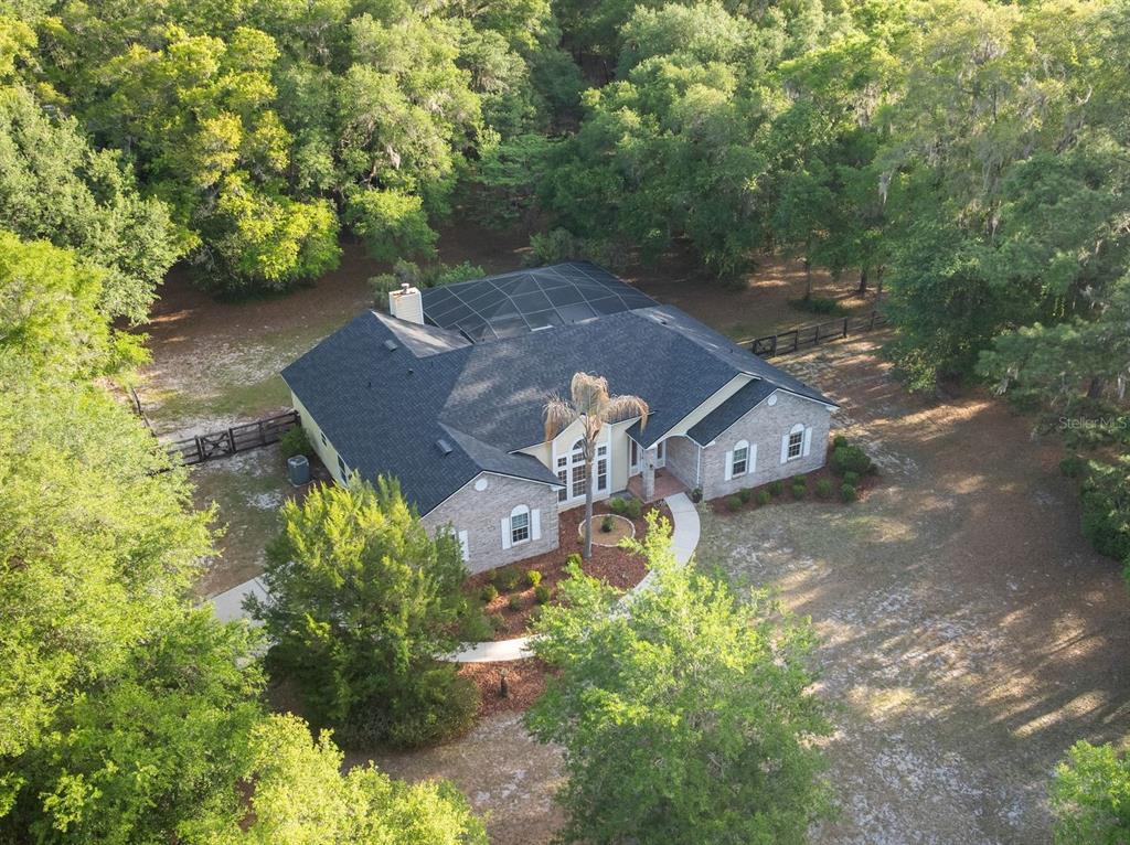 An aerial view shows a brick house with a dark shingled roof and screened-in patio — 8600 SW 103RD AVENUE, GAINESVILLE, FL