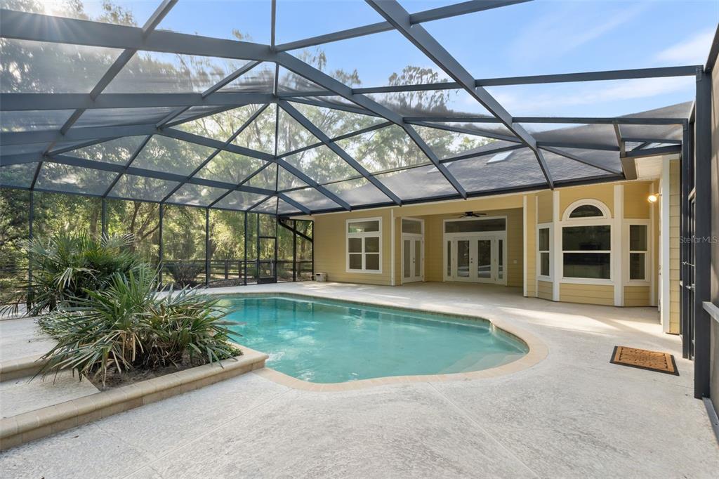 A screened-in pool area with a concrete deck and a yellow house exterior — 8600 SW 103RD AVENUE, GAINESVILLE, FL