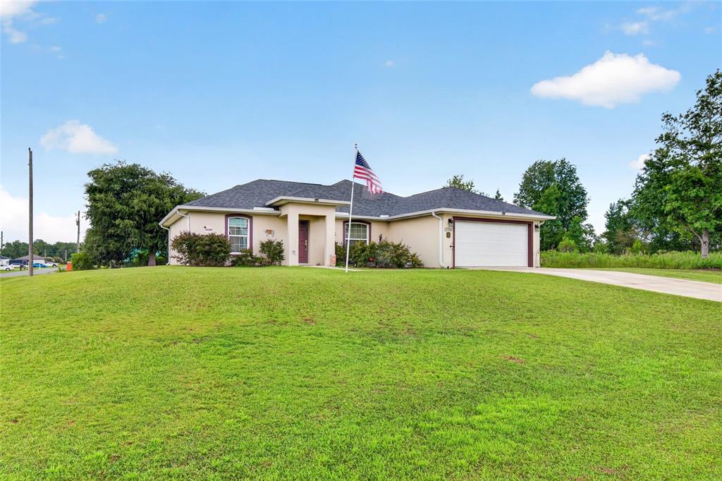 A single-story house with a beige stucco exterior, a two-car garage, and an American flag — 13581 SW 48TH COURT, OCALA, FL
