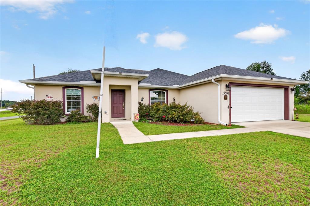 A single-story house with a beige stucco exterior, a dark roof, and a two-car garage — 13581 SW 48TH COURT, OCALA, FL