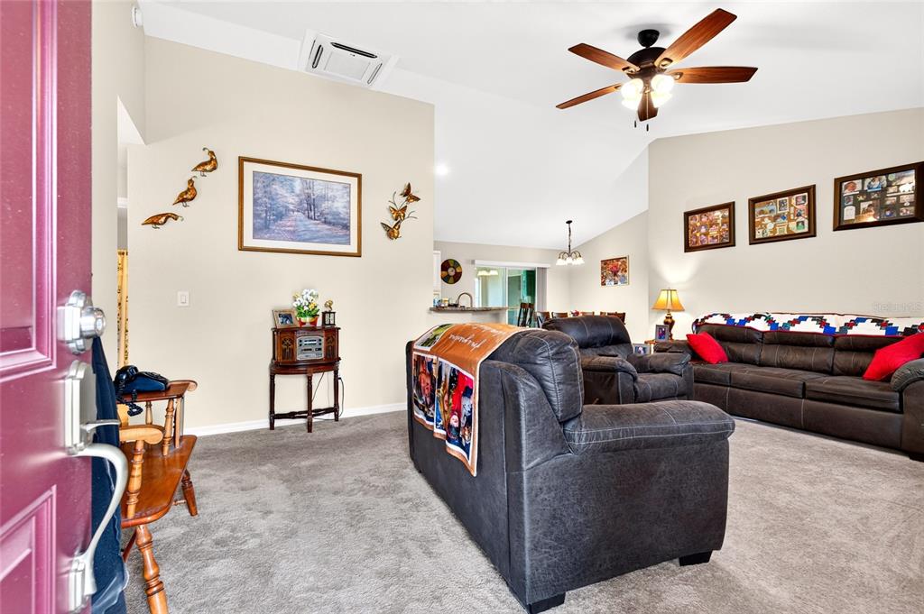 A living room features gray carpeting, dark leather furniture, and a vaulted ceiling with a fan — 13581 SW 48TH COURT, OCALA, FL