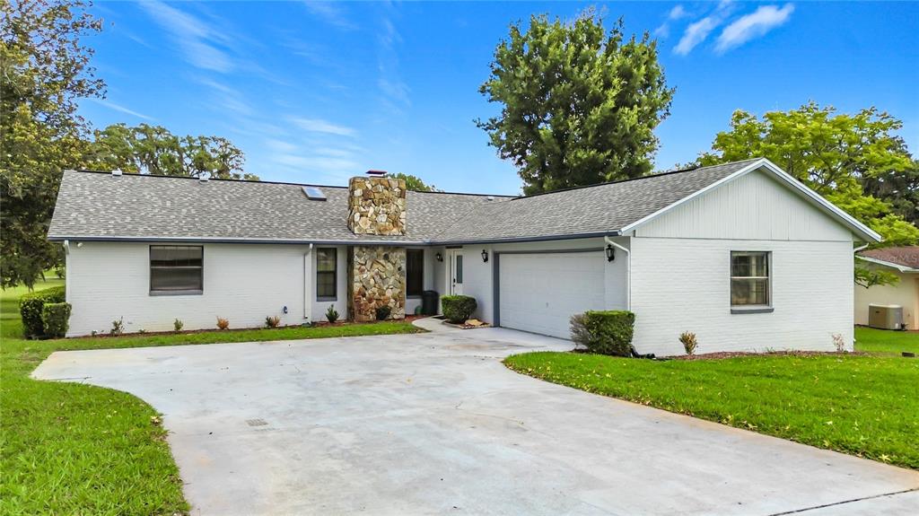 A single-story white brick house features a stone chimney and an attached two-car garage — 8831 E SANDPIPER DRIVE, INVERNESS, FL