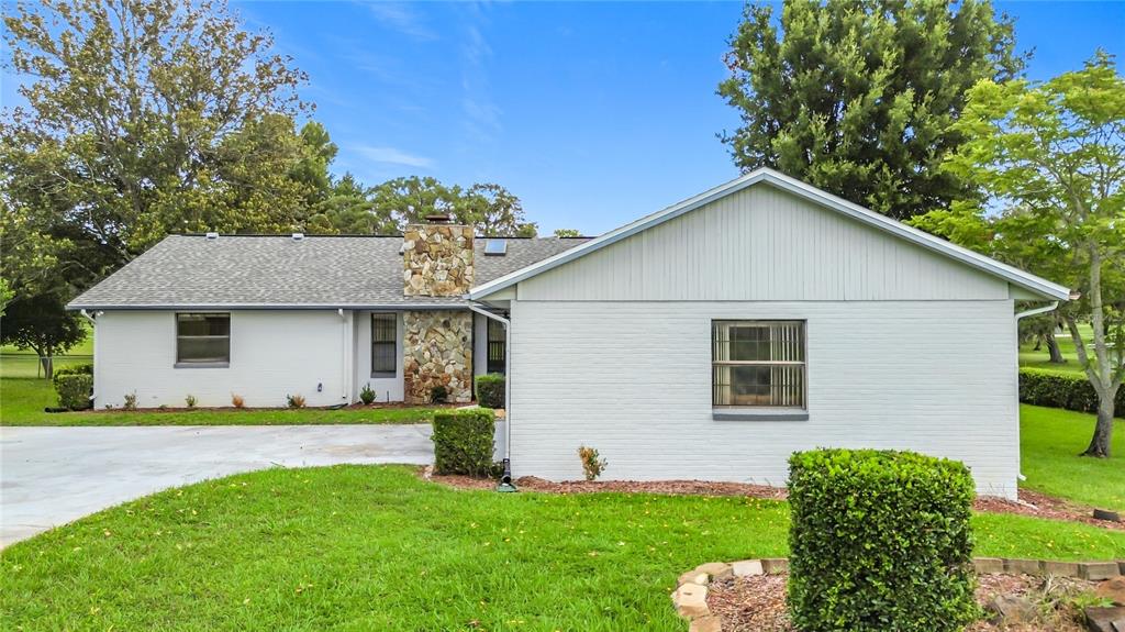 A single-story house with white brick walls, a stone chimney, and a concrete driveway — 8831 E SANDPIPER DRIVE, INVERNESS, FL