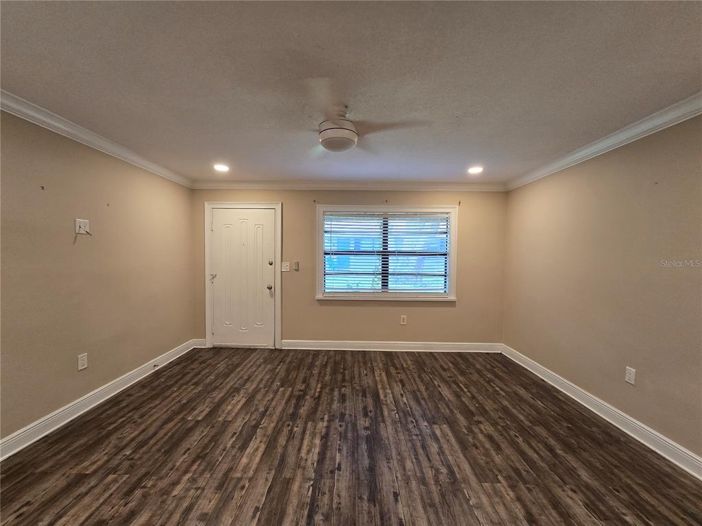 An empty room features wood-look flooring, beige walls, a ceiling fan, and a single window — 447 6TH  NE AVENUE, LARGO, FL