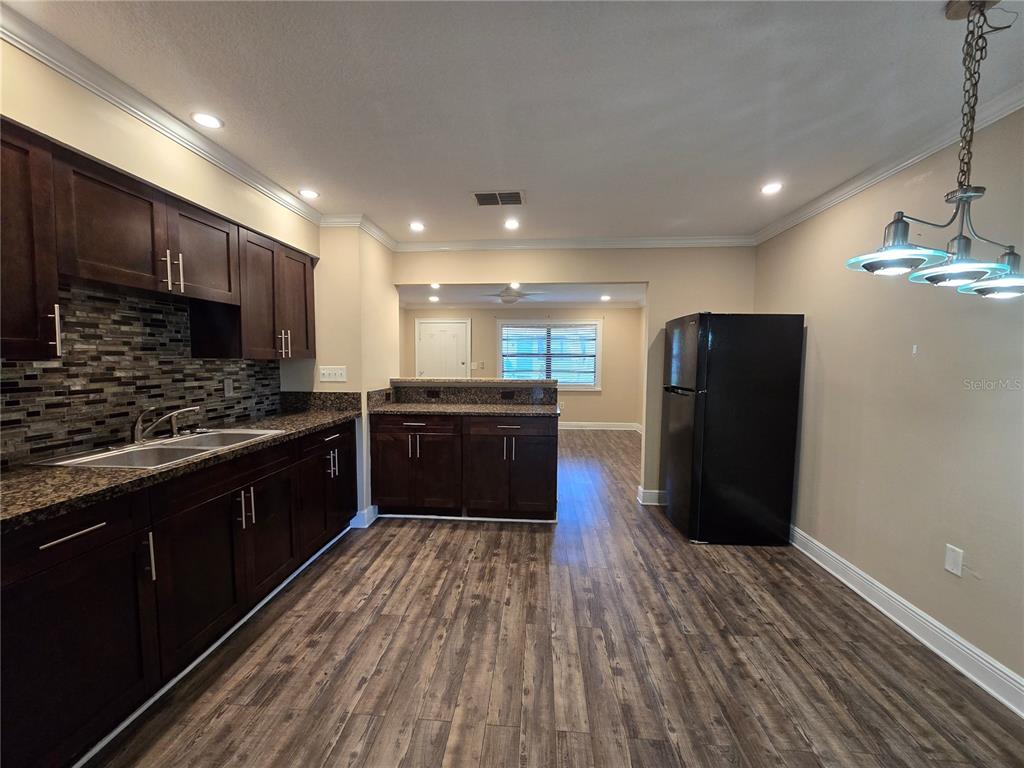 A kitchen with dark wood cabinets, granite countertops, a tiled backsplash, and wood-look flooring — 447 6TH  NE AVENUE, LARGO, FL