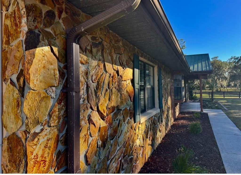 A stone-clad exterior wall features a brown downspout, a window with shutters, and a walkway — 5912 BAILEY ROAD, PLANT CITY, FL