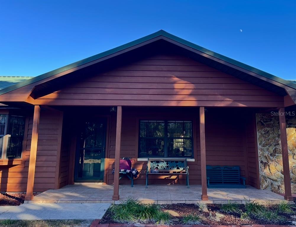 A covered front porch with tiled flooring, wooden siding, and a stone accent wall — 5912 BAILEY ROAD, PLANT CITY, FL