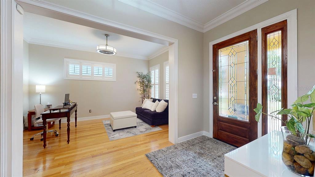 A home office with hardwood floors and a dark sofa sits beside an entryway door — 116 S HESPERIDES STREET, TAMPA, FL