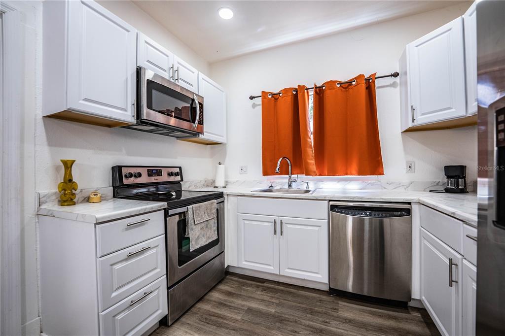 A kitchen featuring white cabinets, stainless steel appliances, marble-look countertops, and orange window curtains — 113 SE PINE AVENUE, FORT MEADE, FL