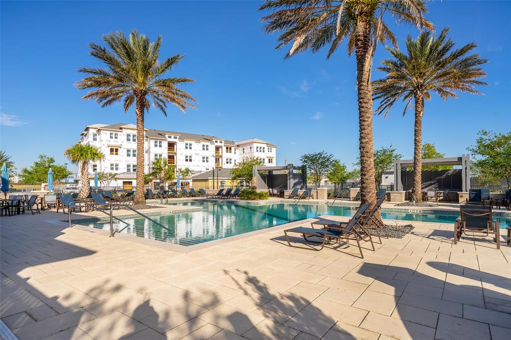 A swimming pool with lounge chairs and palm trees sits in front of a building — 7521 LAUREATE BOULEVARD UNIT 5208, ORLANDO, FL