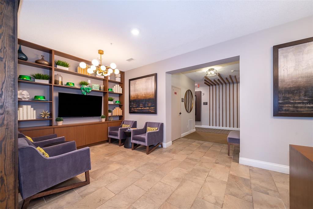 A lounge area features a built-in bookshelf, a television, purple armchairs, and tile flooring — 7521 LAUREATE BOULEVARD UNIT 5208, ORLANDO, FL