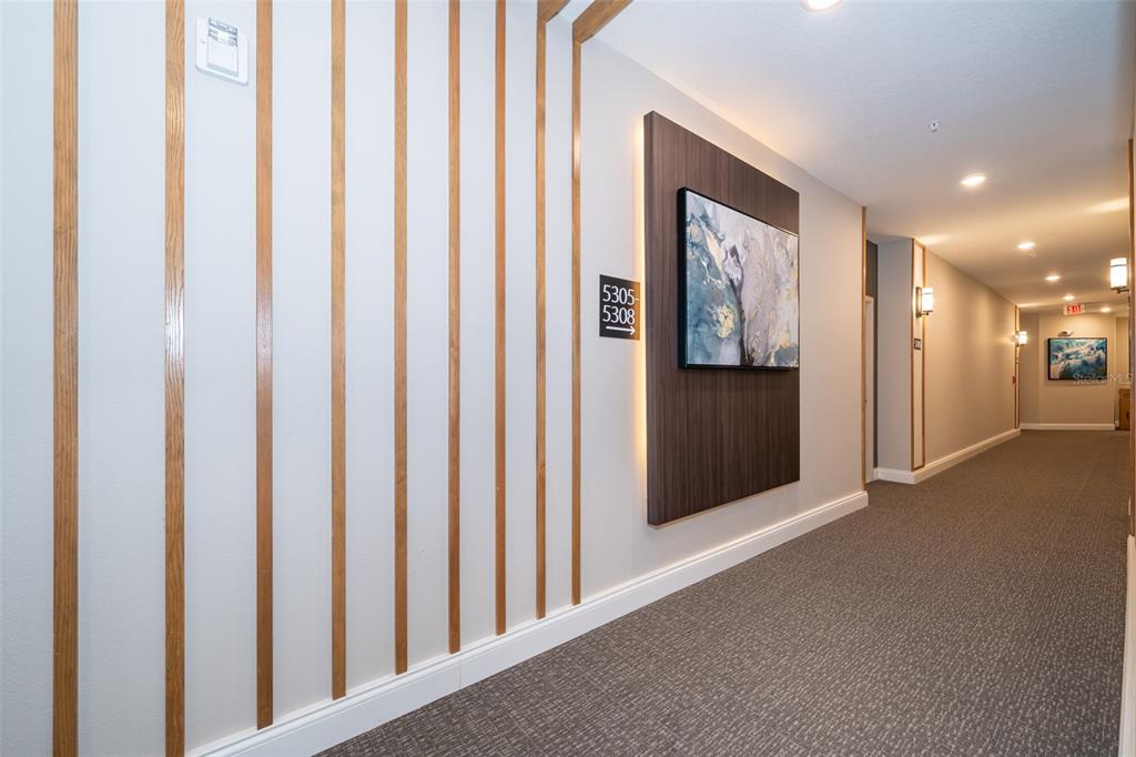 A modern apartment hallway features vertical wood slats, a framed abstract painting, and carpeted flooring — 7521 LAUREATE BOULEVARD UNIT 5208, ORLANDO, FL
