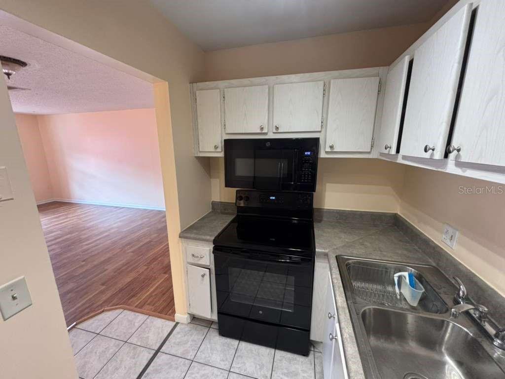 A kitchen features white cabinets, black appliances, a double sink, and tiled flooring — 660 62ND AVENUE N UNIT 1204, ST PETERSBURG, FL