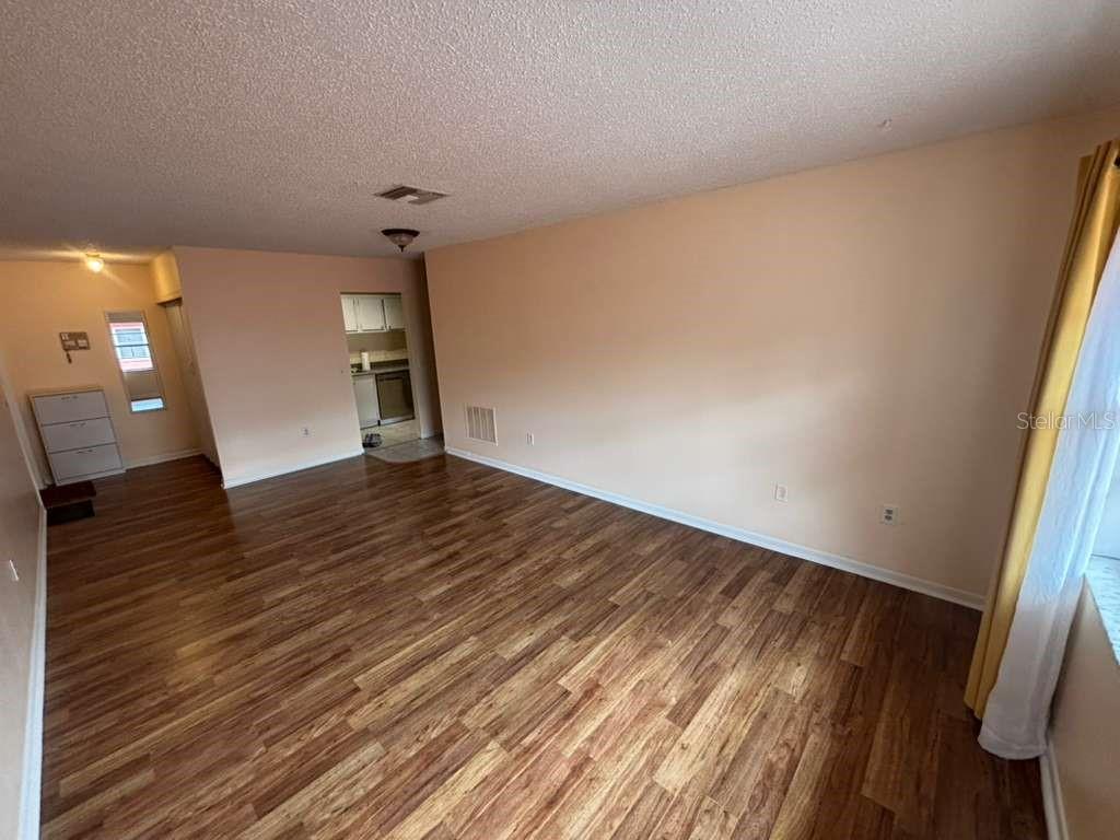 An empty living room features wood-look flooring, light-colored walls, and a view into a kitchen — 660 62ND AVENUE N UNIT 1204, ST PETERSBURG, FL