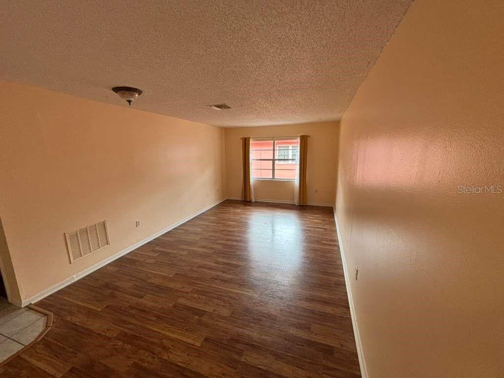An empty room with peach-colored walls, wood-look flooring, and a single window with curtains — 660 62ND AVENUE N UNIT 1204, ST PETERSBURG, FL