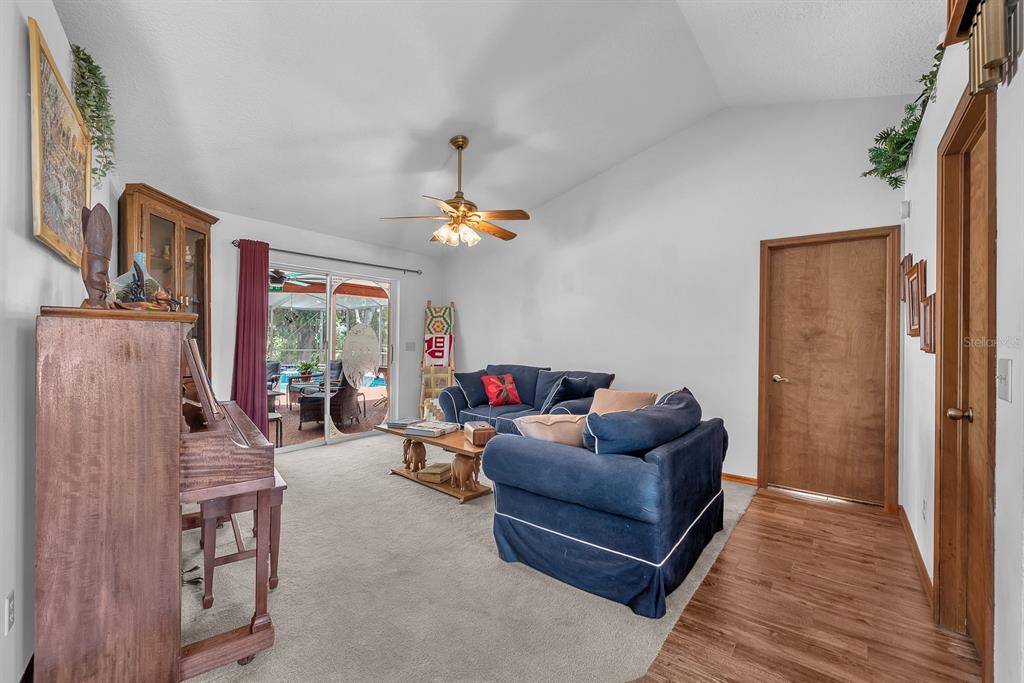 A living room with carpeted floors, blue sofas, a piano, and sliding glass patio doors — 621 PENN NATIONAL ROAD, SEFFNER, FL