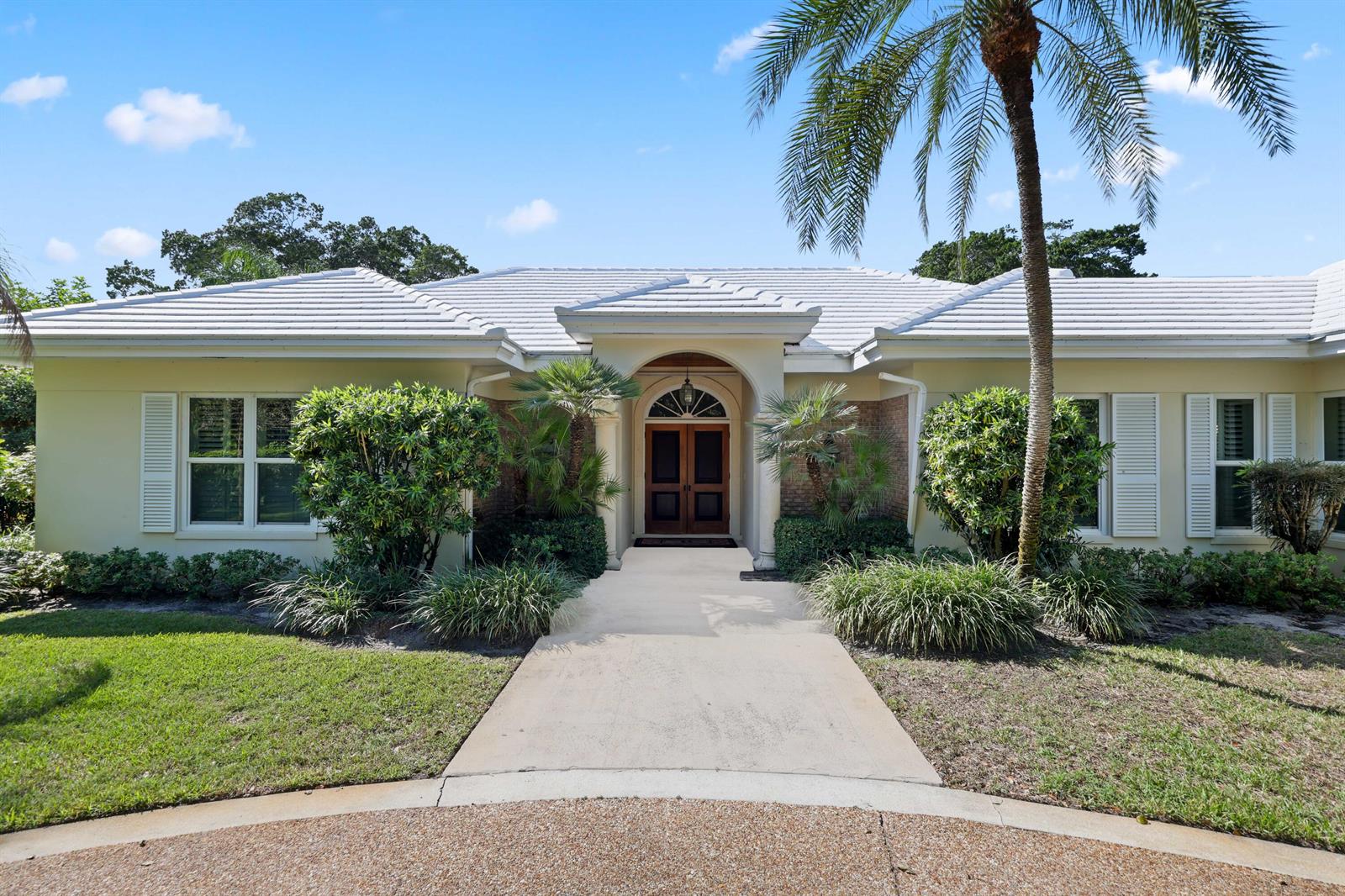 A single-story house with a white tile roof, arched entryway, and a palm tree — 5 Country Road E # A, FL 33436, FL
