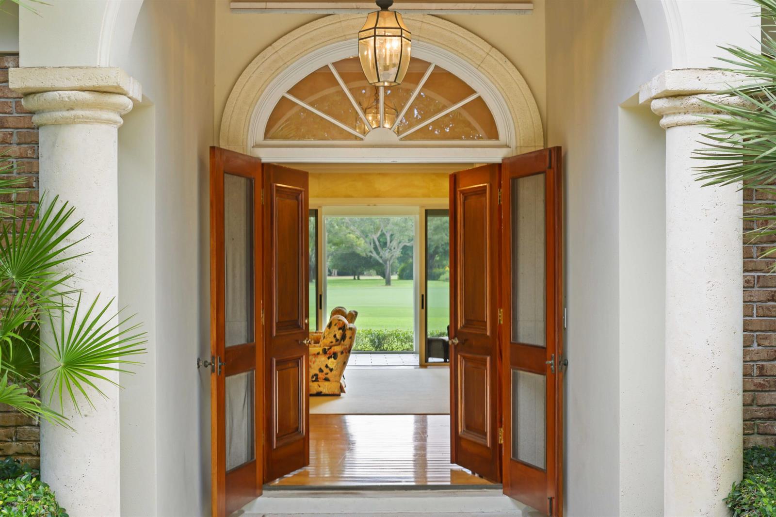 Open double wooden doors reveal a view through a foyer to a green lawn outside — 5 Country Road E # A, FL 33436, FL
