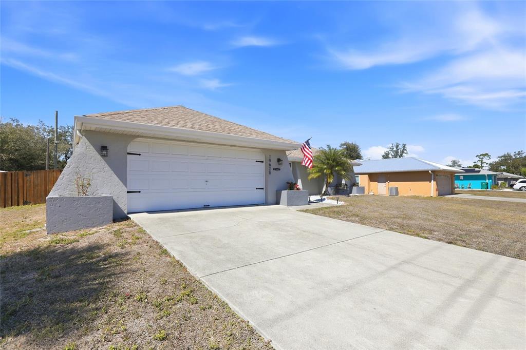 A single-story house with a white garage door, a concrete driveway, and an American flag — 19628 MIDWAY BOULEVARD, PORT CHARLOTTE, FL