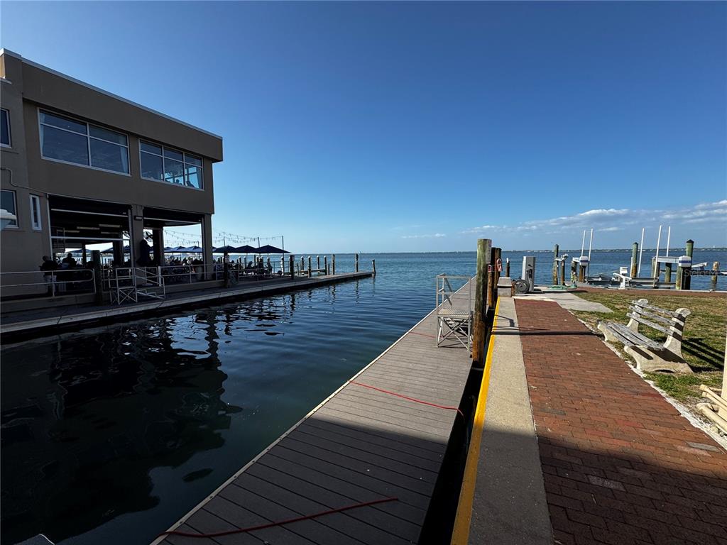 A wooden dock extends into the water beside a restaurant building and brick walkway — 408 GULF OF MEXICO DRIVE UNIT 1332, LONGBOAT KEY, FL