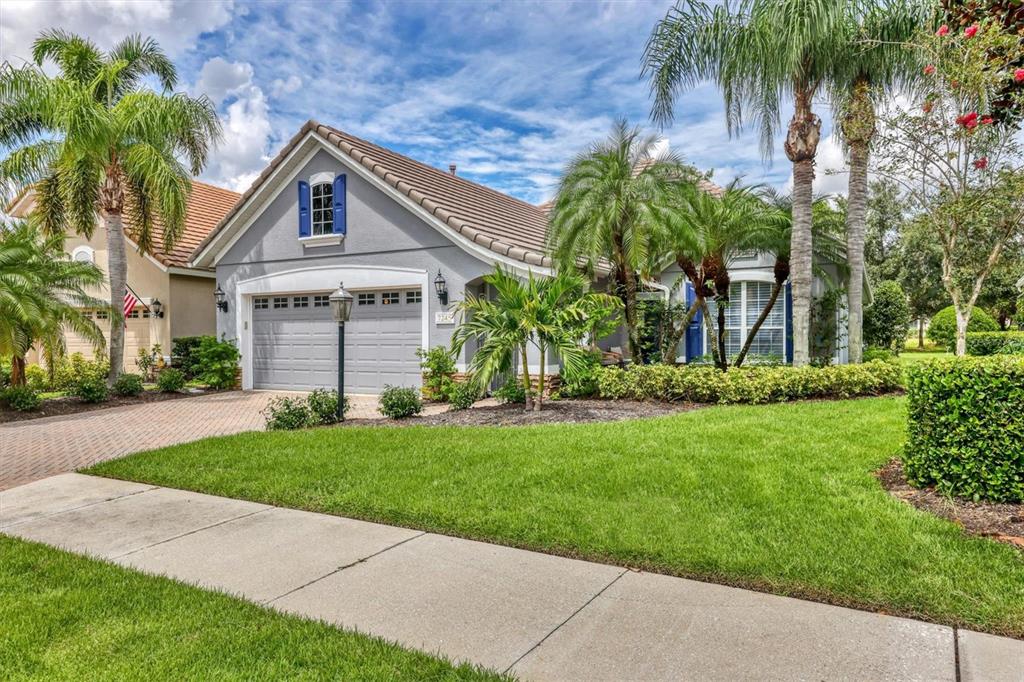 A gray single-story house with a tiled roof, palm trees, and a paved driveway — 7245 ORCHID ISLAND PLACE, LAKEWOOD RANCH, FL