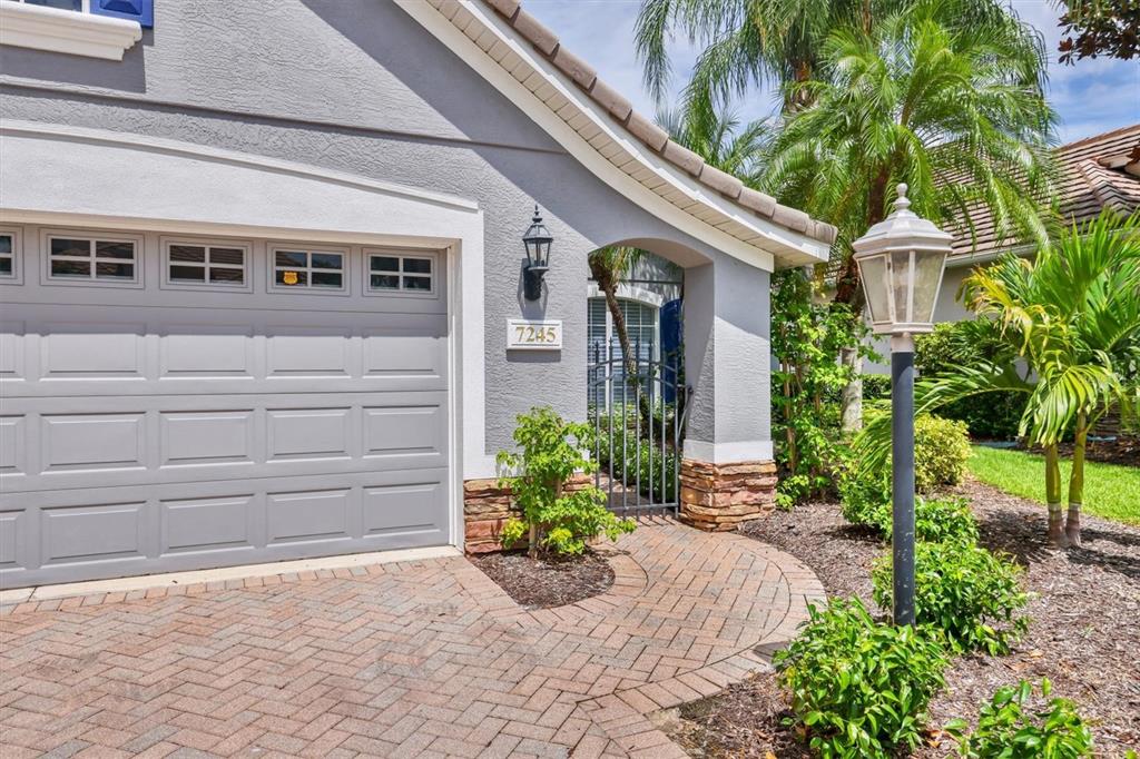 A gray house exterior features a garage, a brick driveway, and a gated entryway — 7245 ORCHID ISLAND PLACE, LAKEWOOD RANCH, FL