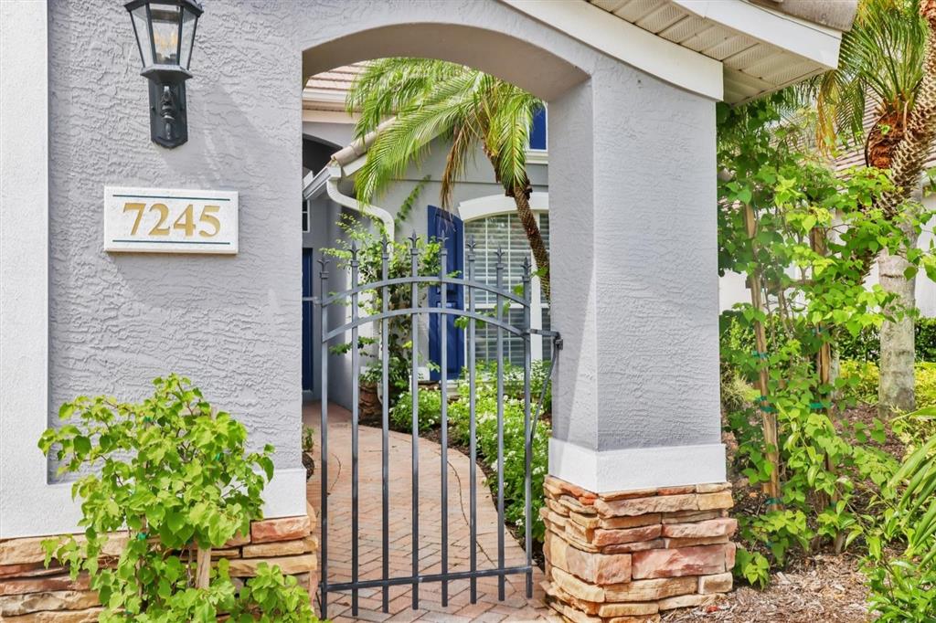 A gray stucco entryway features a stone base, a black metal gate, and a lantern — 7245 ORCHID ISLAND PLACE, LAKEWOOD RANCH, FL