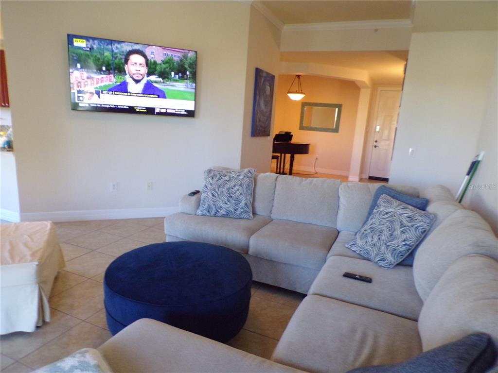 A living room features a sectional sofa, a blue ottoman, and a wall-mounted television — 94 VIVANTE BOULEVARD UNIT 302/9432, PUNTA GORDA, FL
