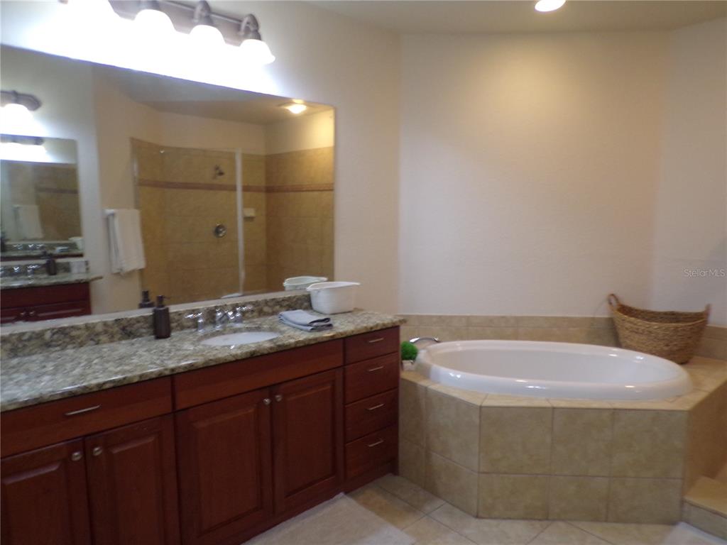 A bathroom features a granite-topped vanity, wooden cabinets, a soaking tub, and a tiled shower — 94 VIVANTE BOULEVARD UNIT 302/9432, PUNTA GORDA, FL