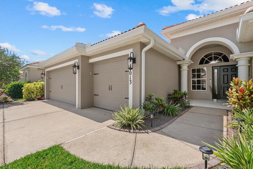 The exterior of a beige house features a two-car garage and a covered entryway — 9013 KINGSBURY PLACE, BRADENTON, FL