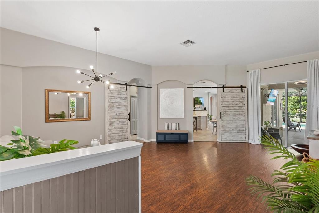 A living room features wood-look flooring, two sliding barn doors, and a modern sputnik chandelier — 9013 KINGSBURY PLACE, BRADENTON, FL