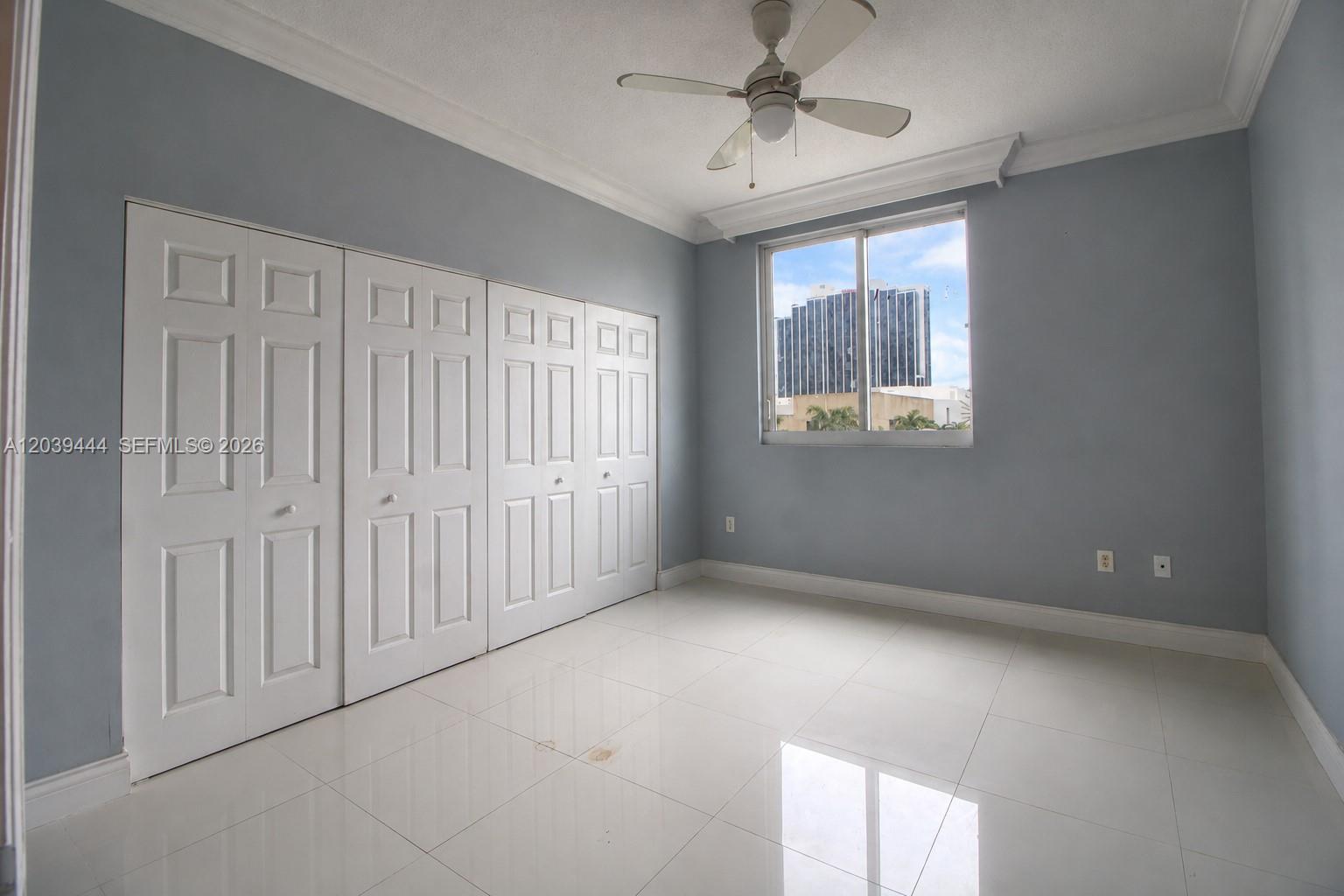 An empty bedroom features light blue walls, white tile flooring, a ceiling fan, and closets — 275 NE 18th St # 504, Miami FL 33132, MIAMI, FL