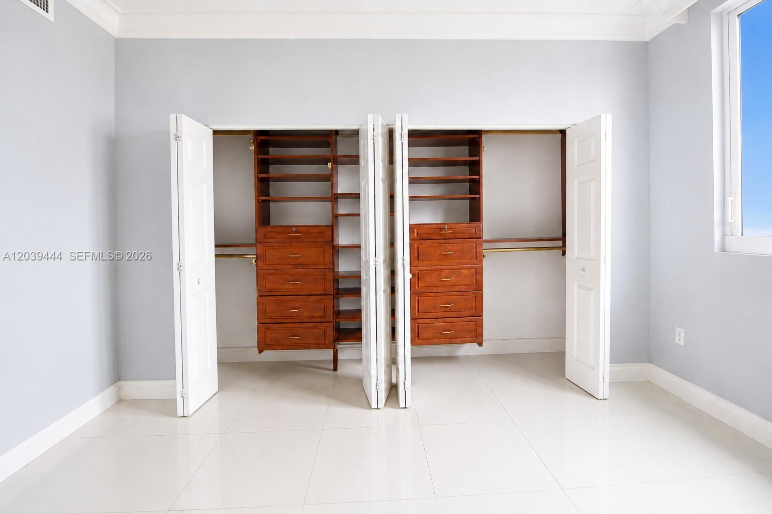 A bedroom features a double closet with built-in wooden shelving and drawers against light walls — 275 NE 18th St # 504, Miami FL 33132, MIAMI, FL