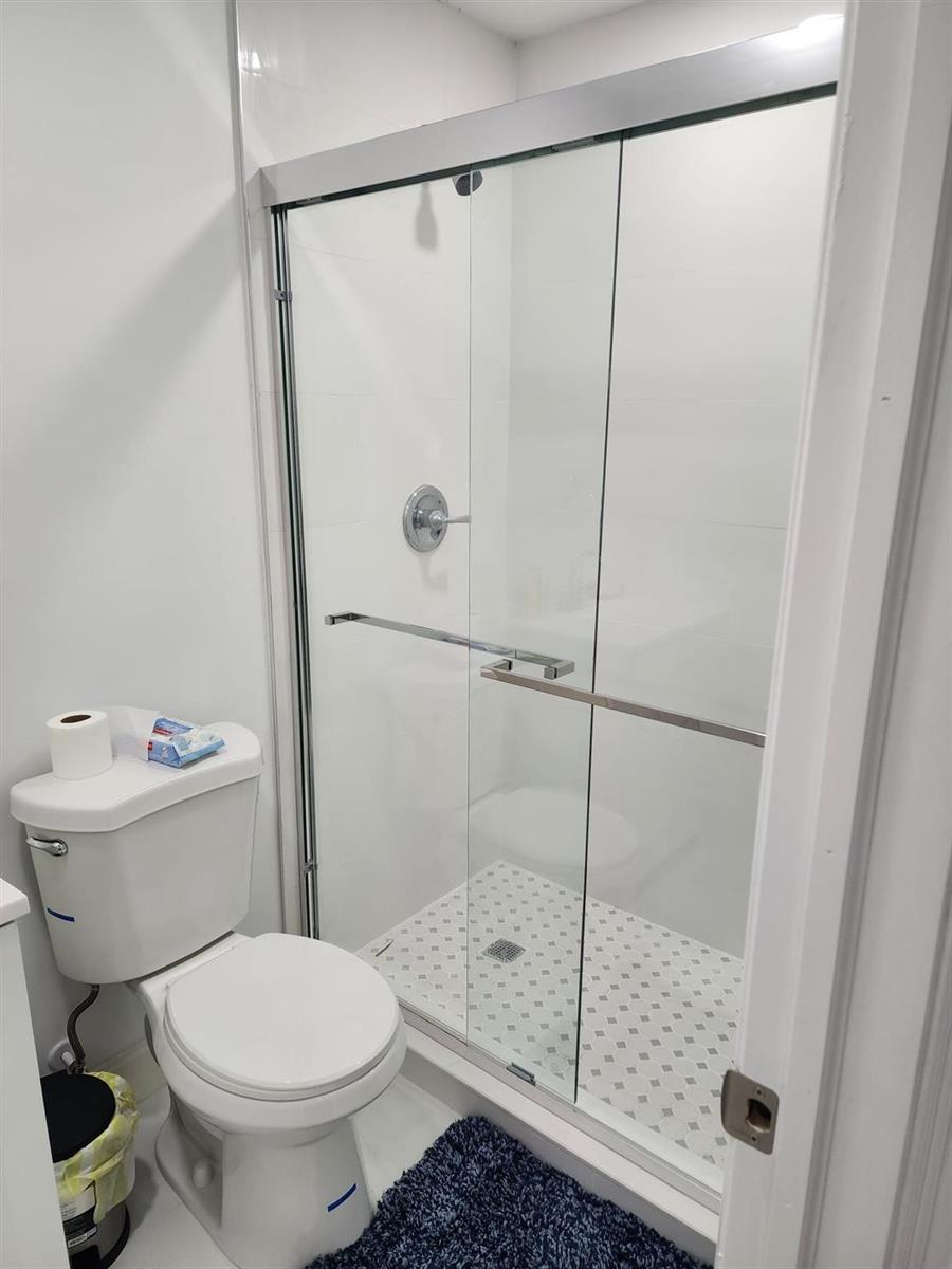 A bathroom features a white toilet next to a glass-enclosed shower with tiled flooring — 320 NW 4th Avenue # 4, Deerfield Beach FL 33441, DEERFIELD BEACH, FL