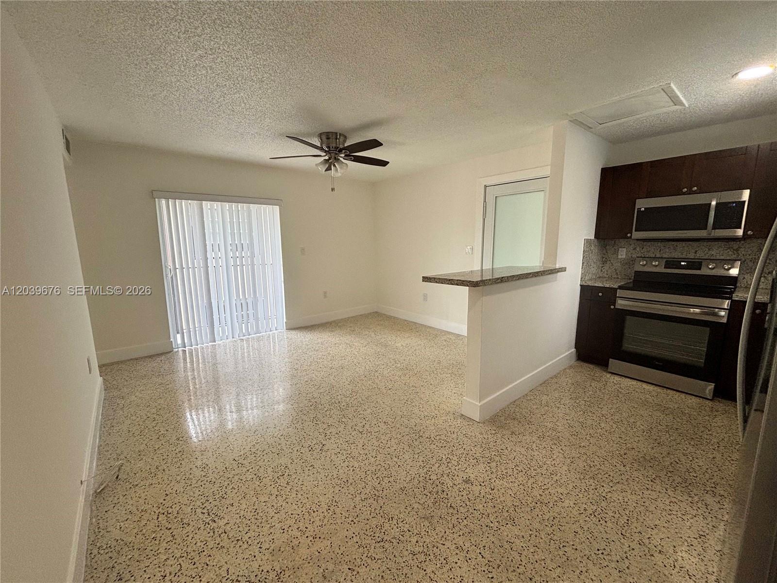 An open-concept room features a kitchen with dark cabinets, stainless appliances, and speckled flooring — 458 E 31st St # 3, Hialeah FL 33013, HIALEAH, FL