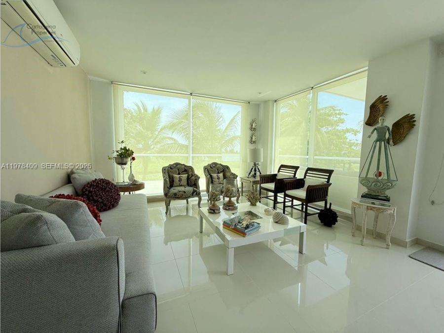 A bright living room features white tile floors, a sofa, armchairs, and floor-to-ceiling windows — 1 Karibana Beach & Golf Condominium # 202, 00000, FL