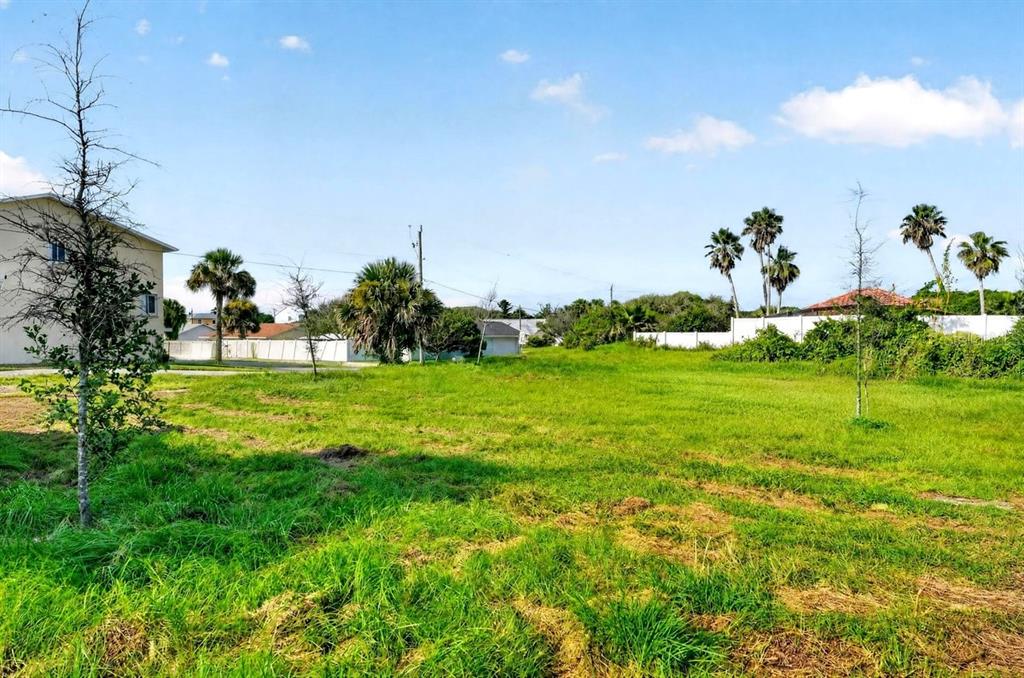 A grassy vacant lot sits in front of multi-story residential buildings under a blue sky — 4738 S ATLANTIC AVENUE, PONCE INLET, FL