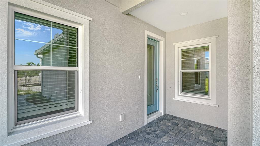 A covered porch features gray stucco walls, a blue front door, and dark paver flooring — 27492 JANZEN COURT, ENGLEWOOD, FL