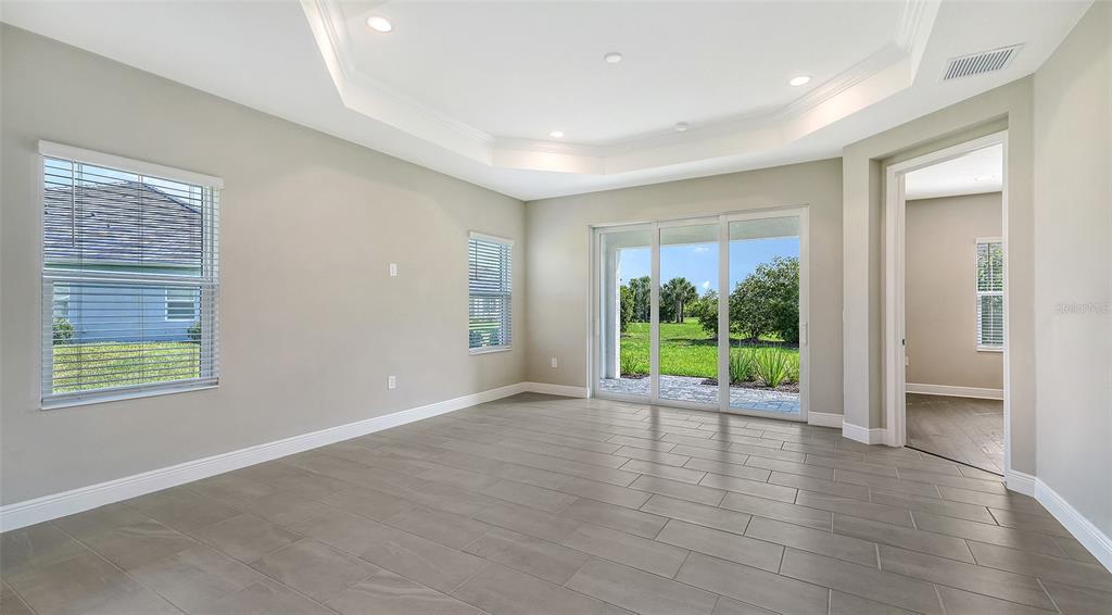An empty room with light gray walls, tile flooring, a tray ceiling, and sliding glass doors — 27492 JANZEN COURT, ENGLEWOOD, FL
