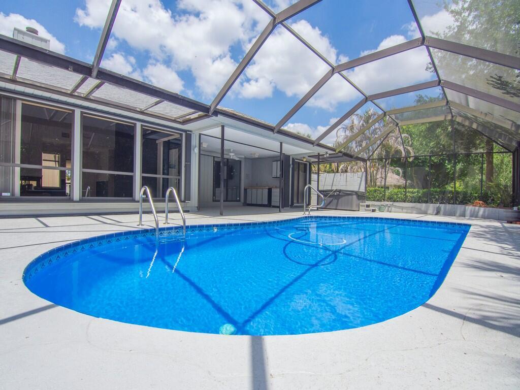 A swimming pool with a metal ladder sits inside a screened-in patio area — 1070 47th Avenue SW, Vero Beach FL 32968, VERO BEACH, FL