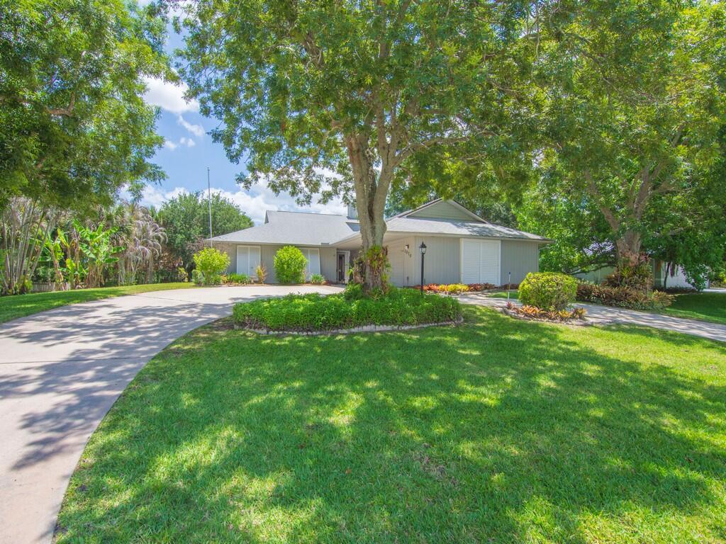 A single-story house with gray siding and a circular driveway sits behind a large tree — 1070 47th Avenue SW, Vero Beach FL 32968, VERO BEACH, FL