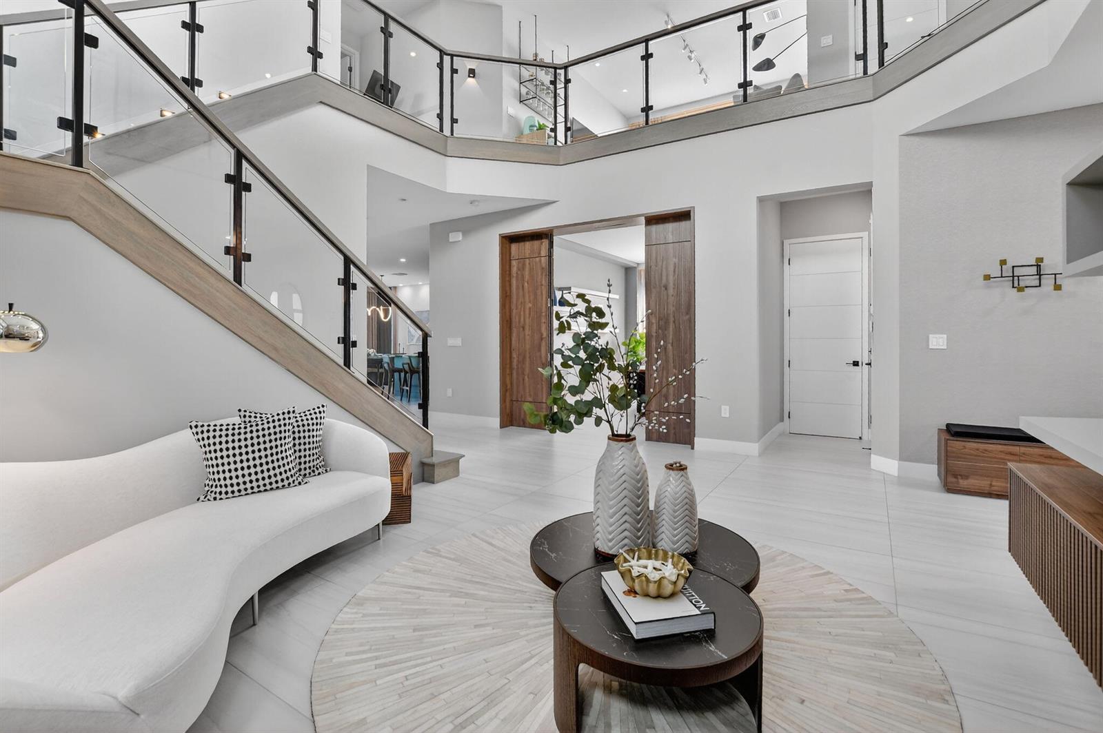 A modern living area features a curved white sofa, tiered coffee tables, and a staircase — 17080 Teton River Road, Boca Raton FL 33496, BOCA RATON, FL