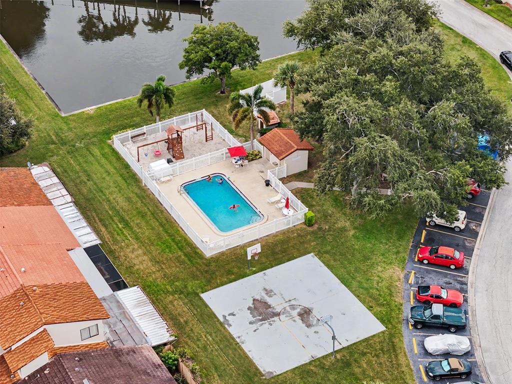 An aerial view shows a swimming pool, playground, basketball court, and parking lot near a lake — 7360 ULMERTON ROAD UNIT 2B, LARGO, FL