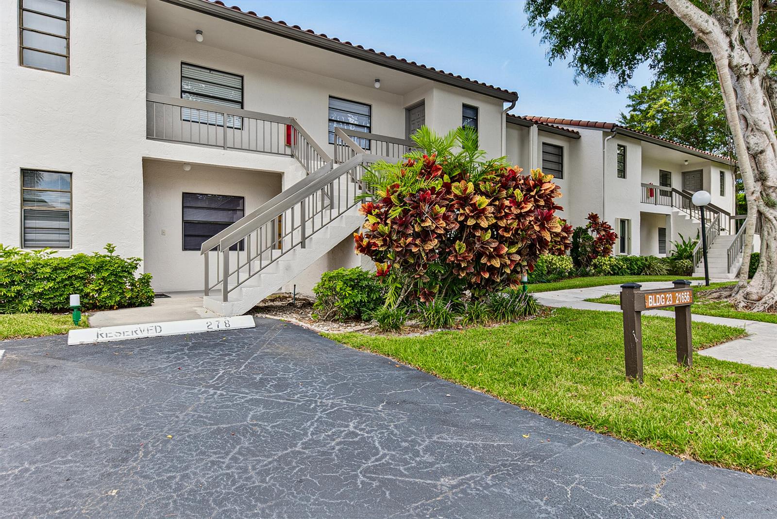 A two-story apartment building features a staircase, a parking space, and a large croton plant — 21656 Juego Circle S # 23f, Boca Raton FL 33433, BOCA RATON, FL